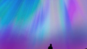 Silueta di una persona in cima a una collina, con vista sull'aurora boreale.