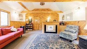 A cozy room with a wooden ceiling, a fireplace, a red sofa, a patterned armchair, and a blue patterned rug.