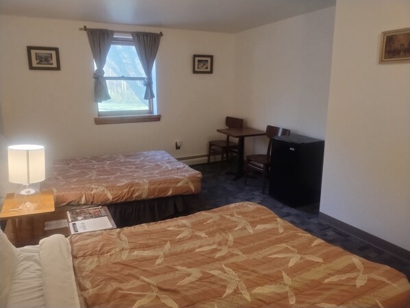 Habitación de hotel con dos camas, un escritorio, una silla, un refrigerador y una ventana con cortinas.