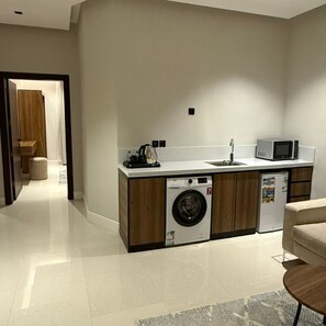 A compact kitchen with a washing machine, a microwave, and a sink. - Afal Suites Al Yarmouk  (Riyadh)