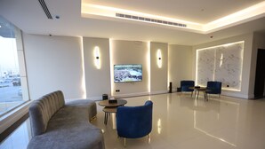 A modern lounge area with a sofa, two blue armchairs, a small round table, and a flat-screen TV mounted on the wall. - Afal Suites Al Yarmouk (Riyadh)