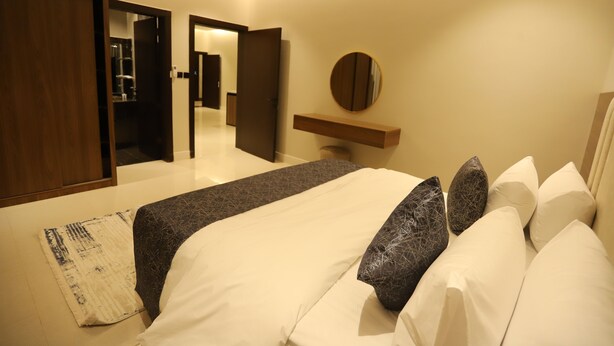 A modern hotel room with a large bed, a bedside table, a mirror, and a wardrobe. - Afal Suites Al Yarmouk (Riyadh)