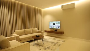 A modern living room with a beige sofa, a coffee table, and a flat-screen TV mounted on the wall. - Afal Suites Al Yarmouk (Riyadh)