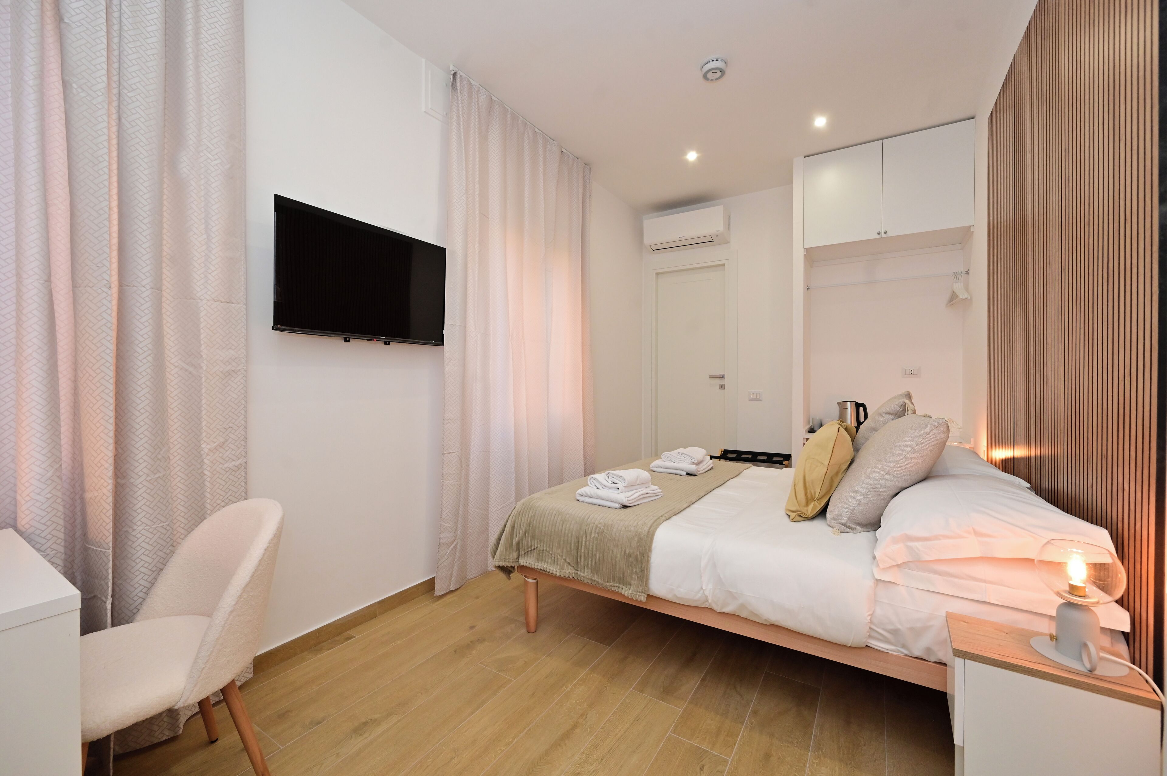 A modern bedroom with a bed, a chair, a TV, and a bedside table with a lamp.