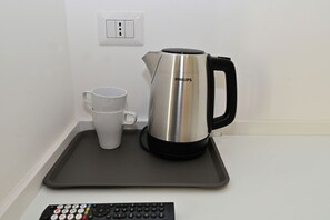 A kettle, a cup, and a remote control on a tray. - Relais Trastevere Station (Rome)