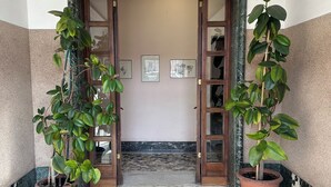 Un vestíbulo con suelo de mármol y dos plantas en macetas a cada lado, que conduce a una puerta de madera con paneles de vidrio.