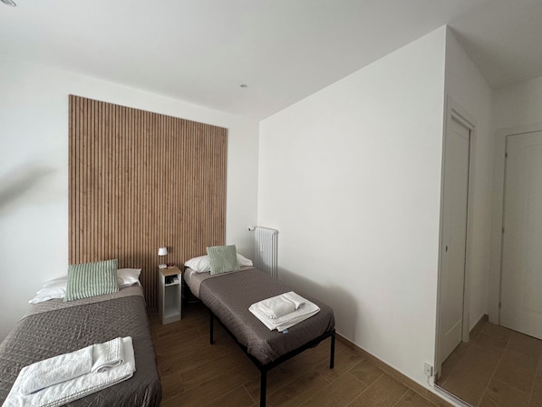 A modern hotel room with two beds, a wooden panel wall, a bedside table with a lamp, and a radiator. - Relais Trastevere Station (Rome)