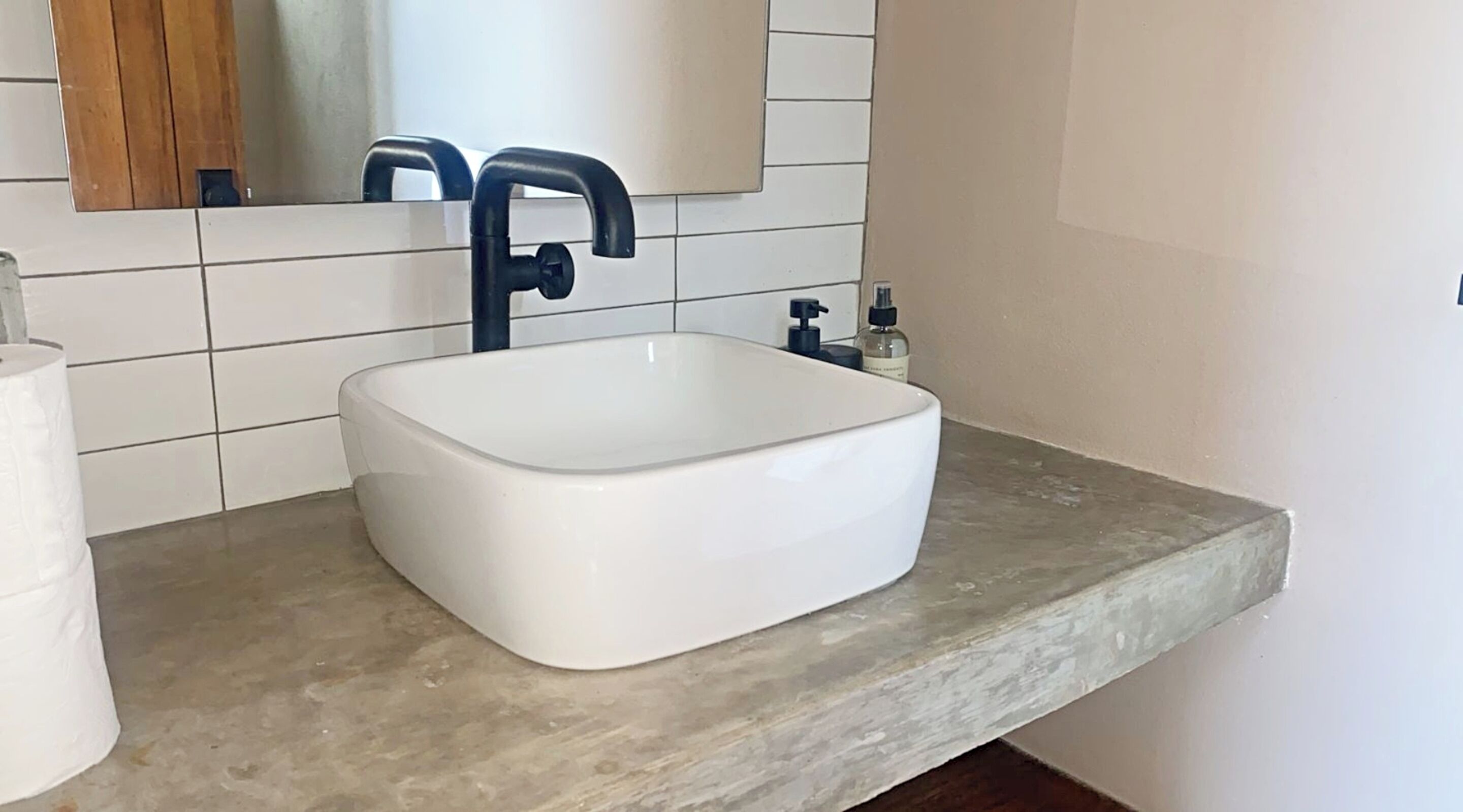 Un baño con lavamanos blanco, grifo oscuro y un espejo encima.