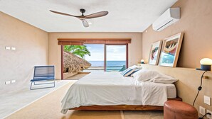 A bedroom with a bed, a ceiling fan, a window with a view of the ocean, and a chair. - Casa Ventana al Mar San Xoaquin (Puerto Vallarta)