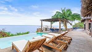 A poolside area with lounge chairs, a pergola, and a view of the ocean. - Casa Ventana al Mar San Xoaquin (Puerto Vallarta)