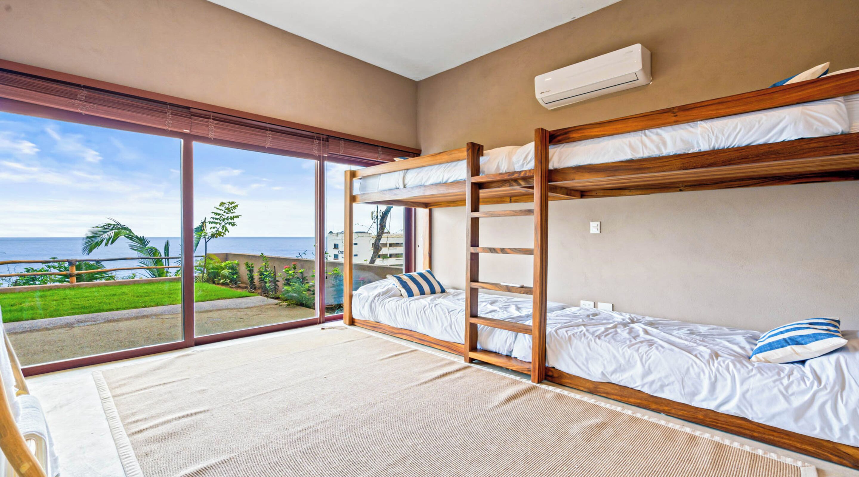 Una habitación con literas, un amplio ventanal corredero que da a un balcón con vistas al océano y un aire acondicionado en la pared.