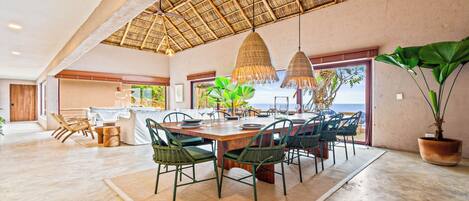 A spacious dining area with a large wooden table, green chairs, and a thatched ceiling.