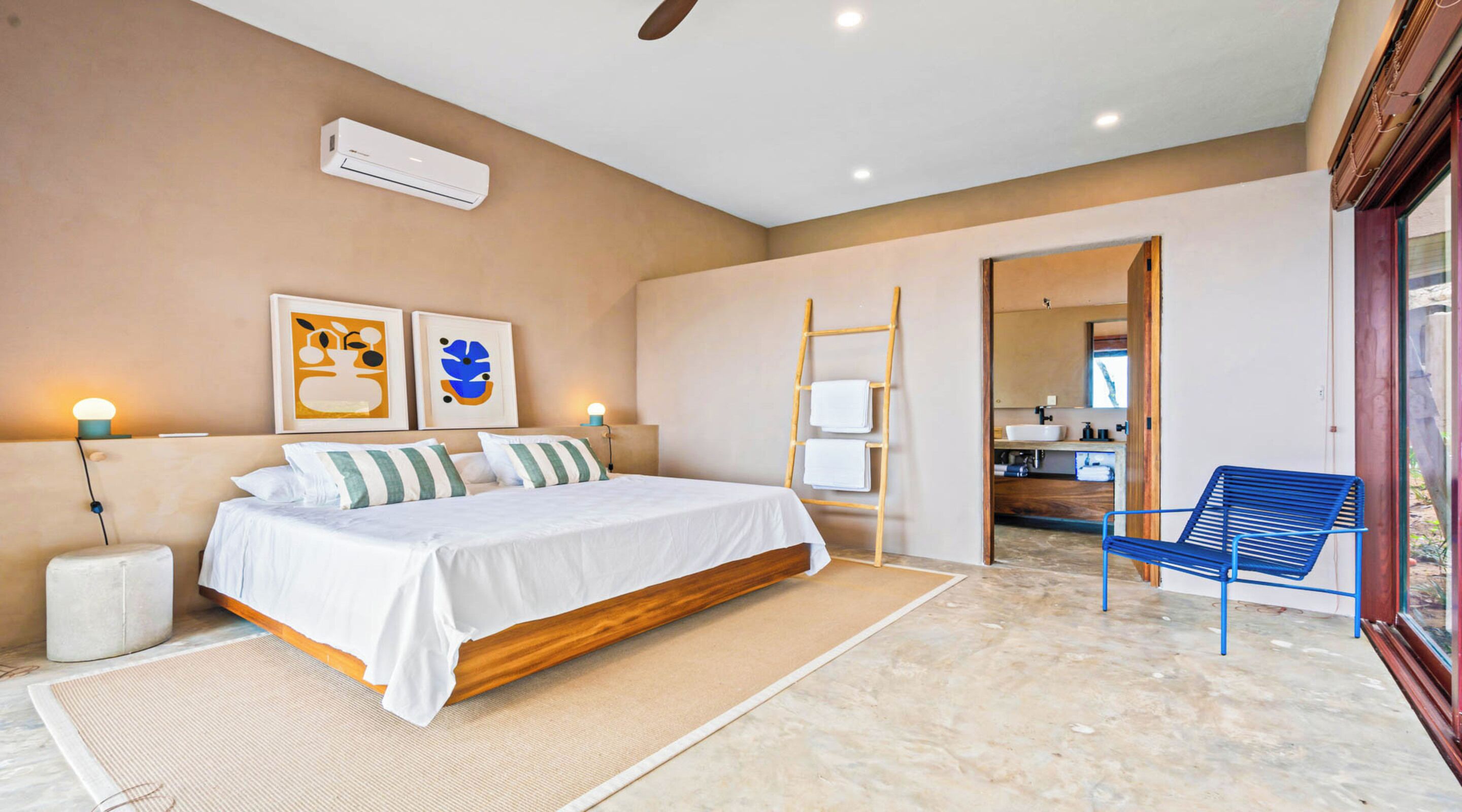 A bedroom with a bed, bedside tables, a chair, a ladder, and artwork on the wall.
