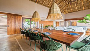 A dining area with a wooden table set for six, surrounded by green chairs, under a thatched roof. - Casa Ventana al Mar San Xoaquin (Puerto Vallarta)