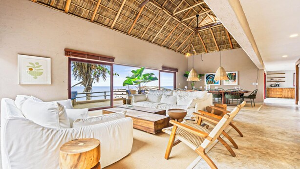 A spacious living area with a large window overlooking the sea, a high ceiling with a thatched roof, and a dining area with modern furniture. - Casa Ventana al Mar San Xoaquin (Puerto Vallarta)