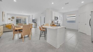 A modern kitchen with white cabinetry, a central island, and a dining area with wooden chairs and a table.