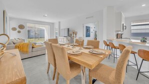 A modern living room with a sofa, a dining table set for four, and a kitchen area with a countertop and chairs.