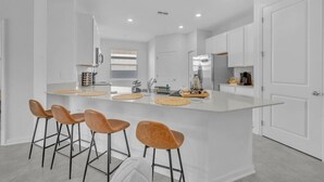 A modern kitchen with a central island, bar stools, and white cabinetry.