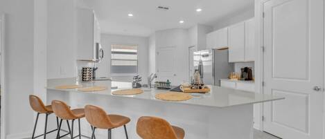 Una cocina moderna con una isla central, taburetes de bar y muebles blancos.