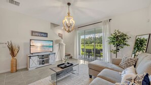 Una sala de estar moderna con televisor, sofá y vistas a un jardín a través de amplios ventanales.