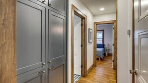 Un couloir avec des portes grises, un plancher en bois et une chambre à coucher avec un lit et une table de chevet.