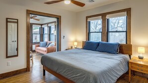 Een slaapkamer met een groot bed, een houten hoofdbord, twee nachtkastjes met lampen, een plafondventilator en uitzicht door een raam.