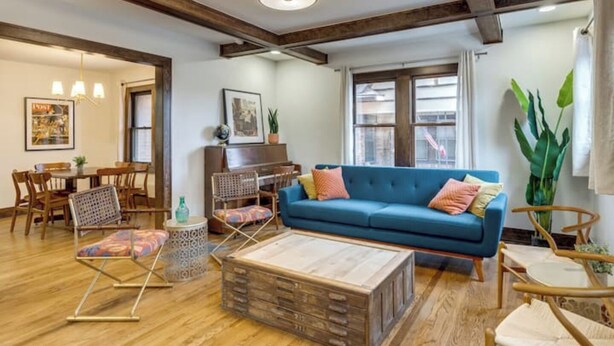 Een ruime woonkamer met een blauwe bank, een houten salontafel en een eethoek met een piano.