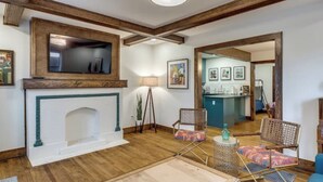Een woonkamer met een open haard, houten balken, een televisie en een keuken in de achtergrond.