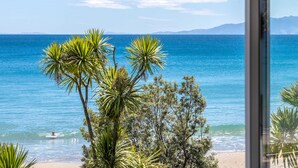 Een uitzicht op het strand met helderblauw water, palmbomen en bergketens in de verte.