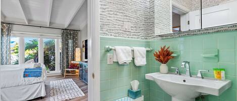 A modern hotel room with a large bed, a view of the outdoors, a bathroom with a green tiled wall, and a sink with toiletries.