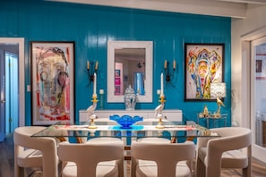 A dining area with a glass table, white chairs, teal walls, and framed artwork.