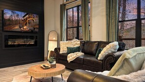 A cozy living room with a fireplace, leather sofa, and large windows.