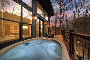 A hot tub on a wooden deck with large windows overlooking a forested area. - NEW Romantic Retreat/HotTub/FirePit/King Bed/Views (Sevierville)