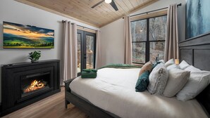 A bedroom with a fireplace, a bed with pillows, a ceiling fan, and a painting on the wall.