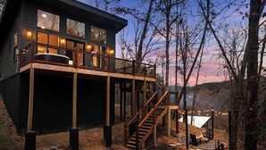 A modern house with a wooden deck, a staircase, and a fire pit area.