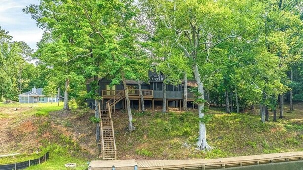 Un chalet au bord du lac, doté d’une terrasse en bois, d’un escalier menant à une autre terrasse, et d’une jetée s’avançant dans l’eau.
