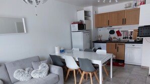 A modern kitchen with white appliances, wooden cabinets, and a dining area with a grey sofa and chairs. - Les Lodges, Apartment Plagne Centre-La Plagne-Tarentaise, 2 rooms 5 people (La Plagne-Tarentaise)