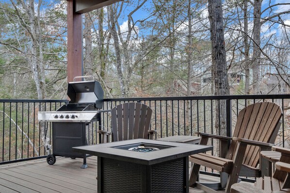 Una terraza con una parrilla, un pozo de fuego y sillas Adirondack.