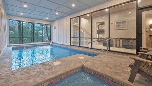 Une piscine intérieure avec des parois en verre transparent, donnant sur les arbres à l’extérieur, et un banc en bois.