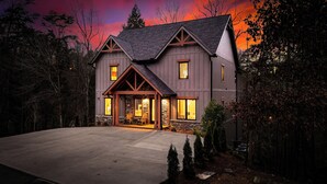 Une grande maison à deux étages, dotée de fondations en pierre et de poutres en bois, et caractérisée par un porche avant spacieux, agrémenté de sièges.
