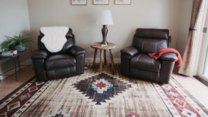 Ein Wohnzimmer mit zwei Ledersesseln, einem runden Holztisch mit Lampe und einem gemusterten Teppich.