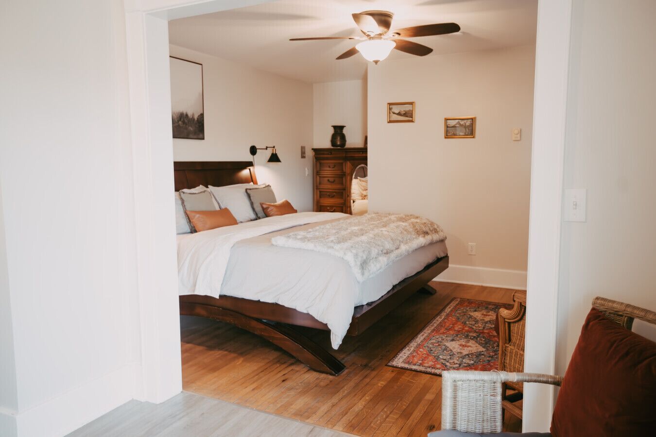 A bedroom with a bed, wooden headboard, a ceiling fan, a nightstand, a lamp, and a small rug.
