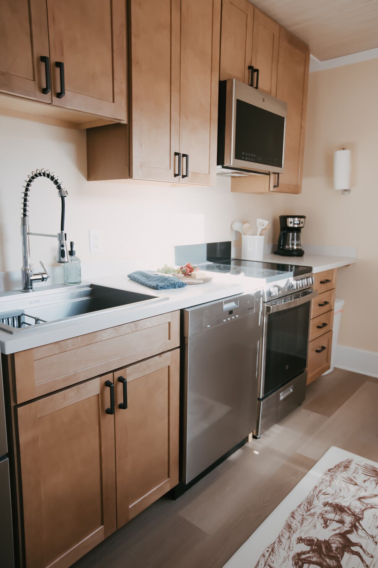 A modern kitchen with wooden cabinets, stainless steel appliances, and a countertop with a coffee maker and utensils.