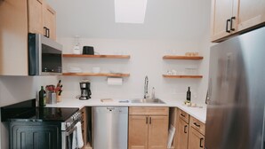 A compact kitchen with wooden cabinets, a stainless steel refrigerator, a dishwasher, and a coffee maker. - Apt. #6 · Goldsmith's River Front Inn - Rock Creek Apartment (Missoula)
