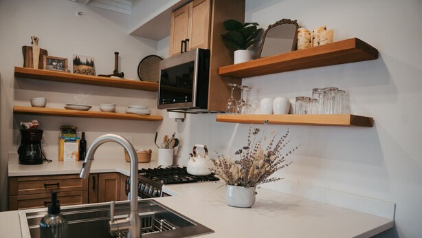 A modern kitchen with wooden shelves, a stainless steel sink, and a white countertop.