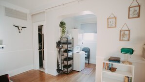 A room with a wooden floor, a red chair, a white shelving unit with books, a green desk lamp, and a framed picture on the wall.