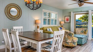 A dining area with a wooden table and white chairs, a green sofa, and a patterned armchair.