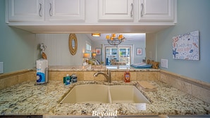 A kitchen with white cabinets, granite countertops, a double sink, and a view to the dining area.
