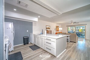 Une cuisine moderne avec des meubles blancs, un îlot central et un coin repas offrant une vue sur l’extérieur.