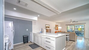 A modern kitchen with white cabinetry, a central island, and a dining area with a view of the outdoors. - The Salty Seahorse | Pet-Friendly Canal Retreat w/ Grill & Deck (Rockport)